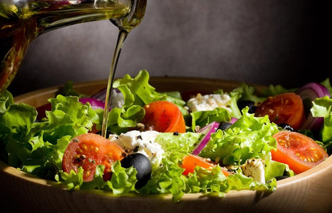 Olive oil being poured onto a fresh salad