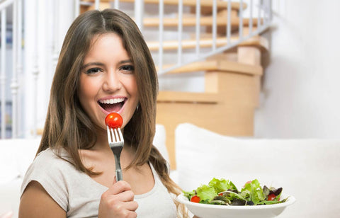 Woman eating a tomato with a bowl of salad